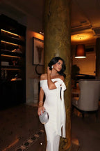 Refinado vestido largo blanco de invitada de boda con hombros descubiertos y lazo decorativo | Maxi